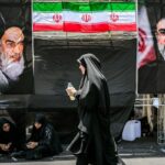 A woman walks past images of Iran's current supreme leader Mojtaba Khamenei (R) and his predecessors, Ali Khamenei (L) and the late Ruhollah Khomeini (2nd-L) on the way to the Grand Mosalla in Tehran on July 5, 2026, for the funeral ceremonies of Ali Khamenei. Photo by Ozan KOSE / AFP via Getty Images.