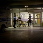 a person wheeled in on an ambulance stretcher outside of a U.S. emergency room at night