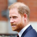 Sir Elton John de terno, gravata e óculos escuros, acenando do lado de fora do Royal Courts of Justice em 2023