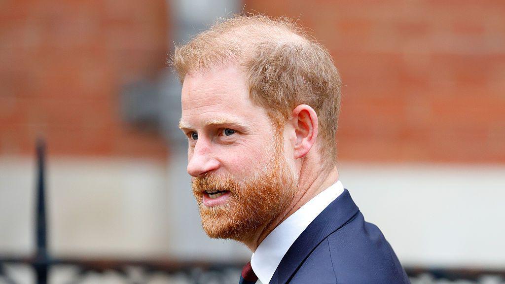 Sir Elton John de terno, gravata e óculos escuros, acenando do lado de fora do Royal Courts of Justice em 2023