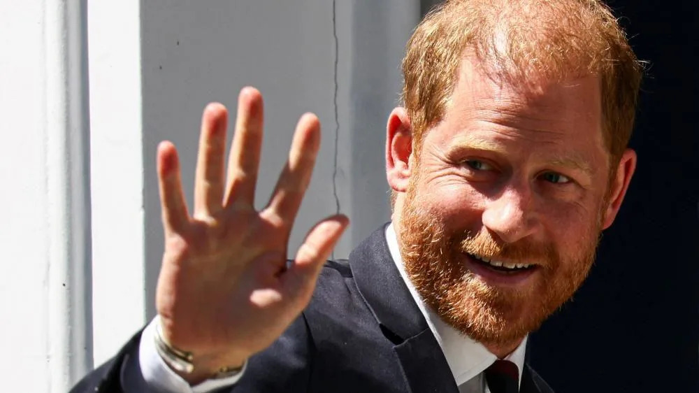 Príncipe Harry jogando futebol em cadeira de rodas, sentado em uma cadeira de rodas preta e vermelha com uma bola entre as pernas