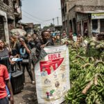 GOMA, REPÚBLICA DEMOCRÁTICA DO CONGO - 24 DE JUNHO: Uma mulher carregando bananas lê um panfleto enquanto trabalhadores do grupo 'U-Report' da UNICEF aumentam a conscientização sobre a transmissão do Ebola no mercado de Alanina em 24 de junho de 2026 em Goma, República Democrática do Congo. Na segunda-feira, as agências da ONU anunciaram que os casos de Ébola na República Democrática do Congo ultrapassaram os 1.000. Embora a capacidade de testagem tenha melhorado recentemente, a vigilância e o rastreio de contactos continuam limitados pela insegurança e pelo acesso restrito na província de Ituri, o centro do actual surto, a norte de Goma. (Foto de Daniel Buuma/Getty Images)