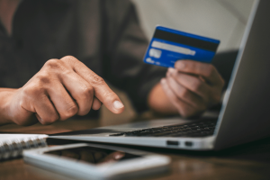 Pessoa que usa um cartão de crédito para fazer um pagamento on-line em um laptop, ilustrando o processamento de pagamentos digitais e transações de jogos de azar on-line. Reclamação da EGBA visa Walletto sobre pagamentos ilegais de jogos de azar na Lituânia