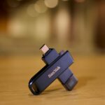 SANDISK Phone Drive para iPhone mostrado em uma mesa com iluminação fora de foco atrás
