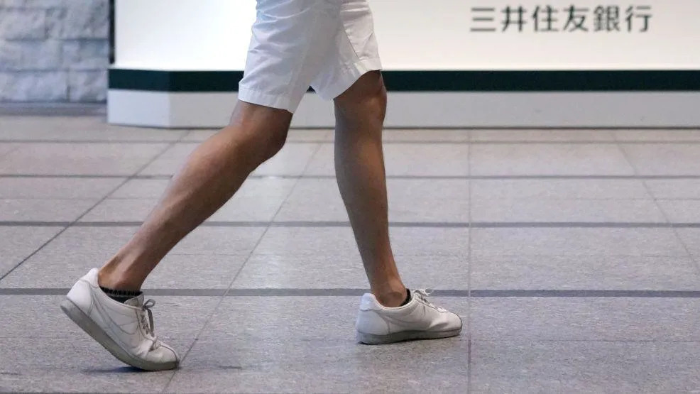 Quatro homens vestindo shorts no escritório em Tóquio, Japão. Três deles em pé, um deles sentado e com os cotovelos apoiados na mesa.