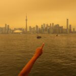 Uma pessoa coloca uma máscara refletida no espelho de uma loja de souvenirs, enquanto a fumaça do incêndio florestal do noroeste de Ontário enche o céu, em Toronto na quarta-feira