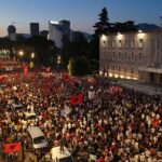 Manifestantes carregam cartazes enquanto se manifestam em frente ao Gabinete do Primeiro Ministro albanês contra a construção de um resort de luxo perto de uma área natural protegida na costa sul da Albânia, em Tirana, em 4 de julho de 2026.