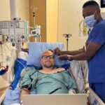 Um homem controla um laptop no corredor de um hospital.