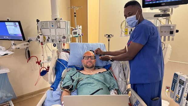 Um homem controla um laptop no corredor de um hospital.