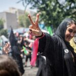 Um iraniano faz um sinal de vitória enquanto está sob água fria pulverizada por funcionários municipais depois de prestar as últimas homenagens ao líder supremo do Irã, aiatolá Ali Khamenei, durante o terceiro dia de suas cerimônias fúnebres, em 6 de julho.