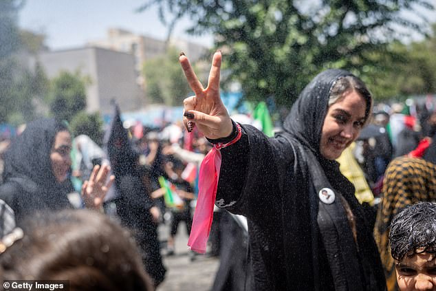 Um iraniano faz um sinal de vitória enquanto está sob água fria pulverizada por funcionários municipais depois de prestar as últimas homenagens ao líder supremo do Irã, aiatolá Ali Khamenei, durante o terceiro dia de suas cerimônias fúnebres, em 6 de julho.